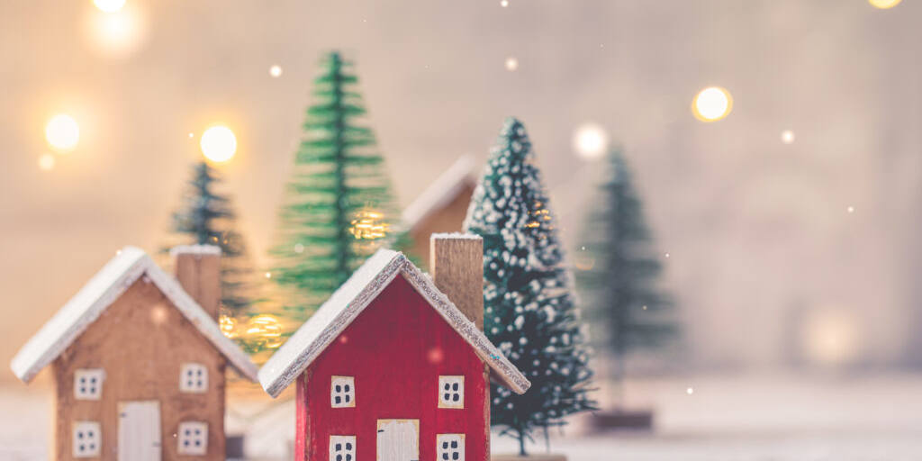 Miniature wooden houses on the snow over blurred Christmas decoration background, toned, postcard concept
