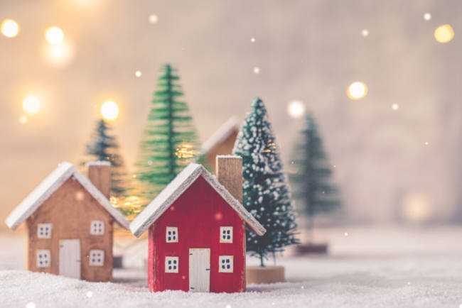 Miniature wooden houses on the snow over blurred Christmas decoration background, toned, postcard concept